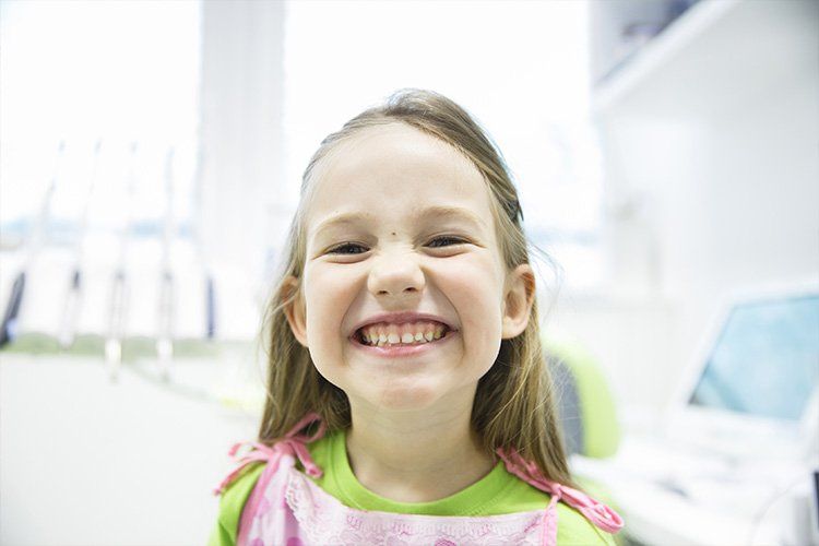 Smiling young girl in a dental office. She wears a pink bib over a green shirt.