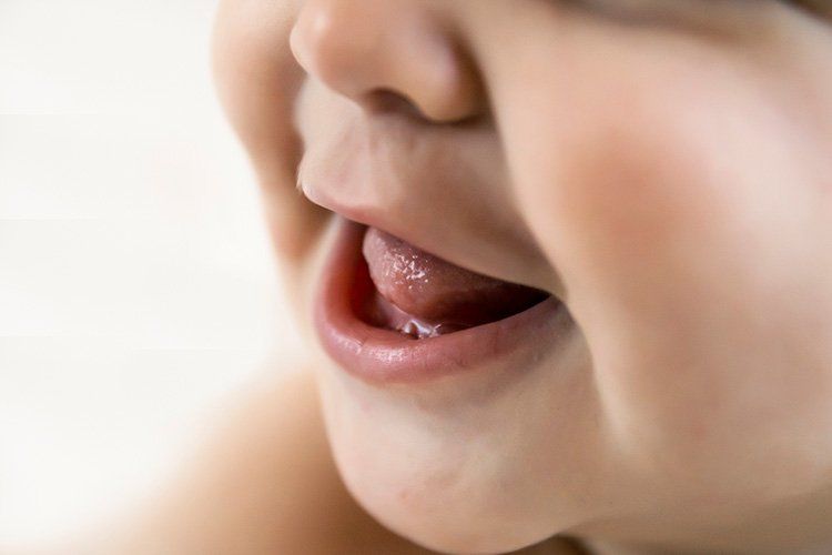 Close-up of a baby's open mouth, tongue visible, pink lips, and soft cheeks.