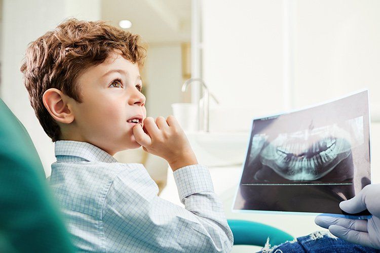 Boy in dentist chair looks at x-ray, thinking. Dental office setting.