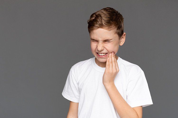 Boy in white shirt holding cheek, showing expression of tooth pain.