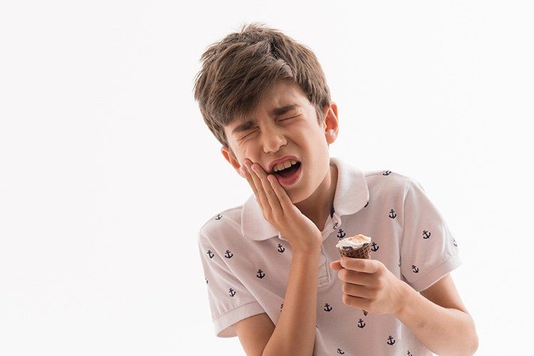 Boy with tooth pain holding an ice cream, clutching his jaw. White background.