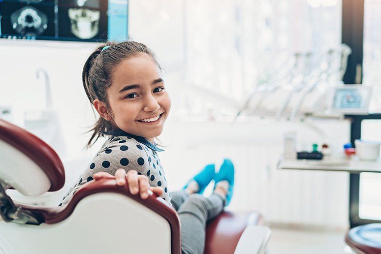 Smiling girl in a dental chair at a dentist's office; window in background.