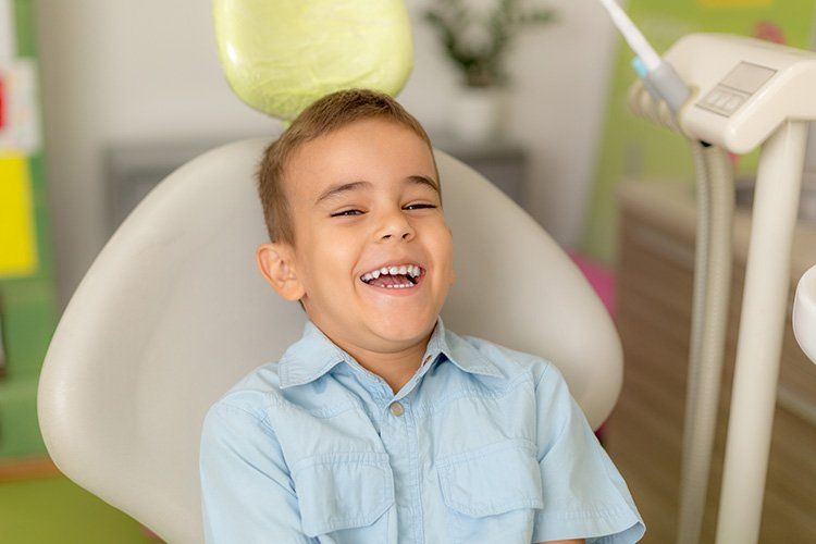 Smiling boy in a dentist's chair, light blue shirt, happy expression, dental office setting.