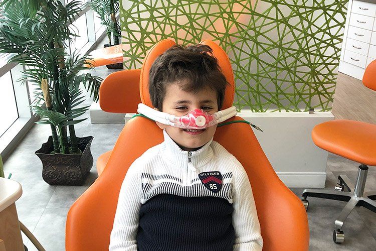 Boy in dental chair with oxygen mask; bright orange, white, and green colors.