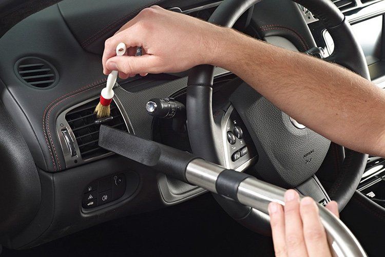 A person is cleaning the dashboard of a car with a vacuum cleaner