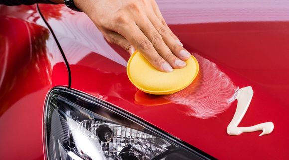A person is polishing a red car with a sponge.