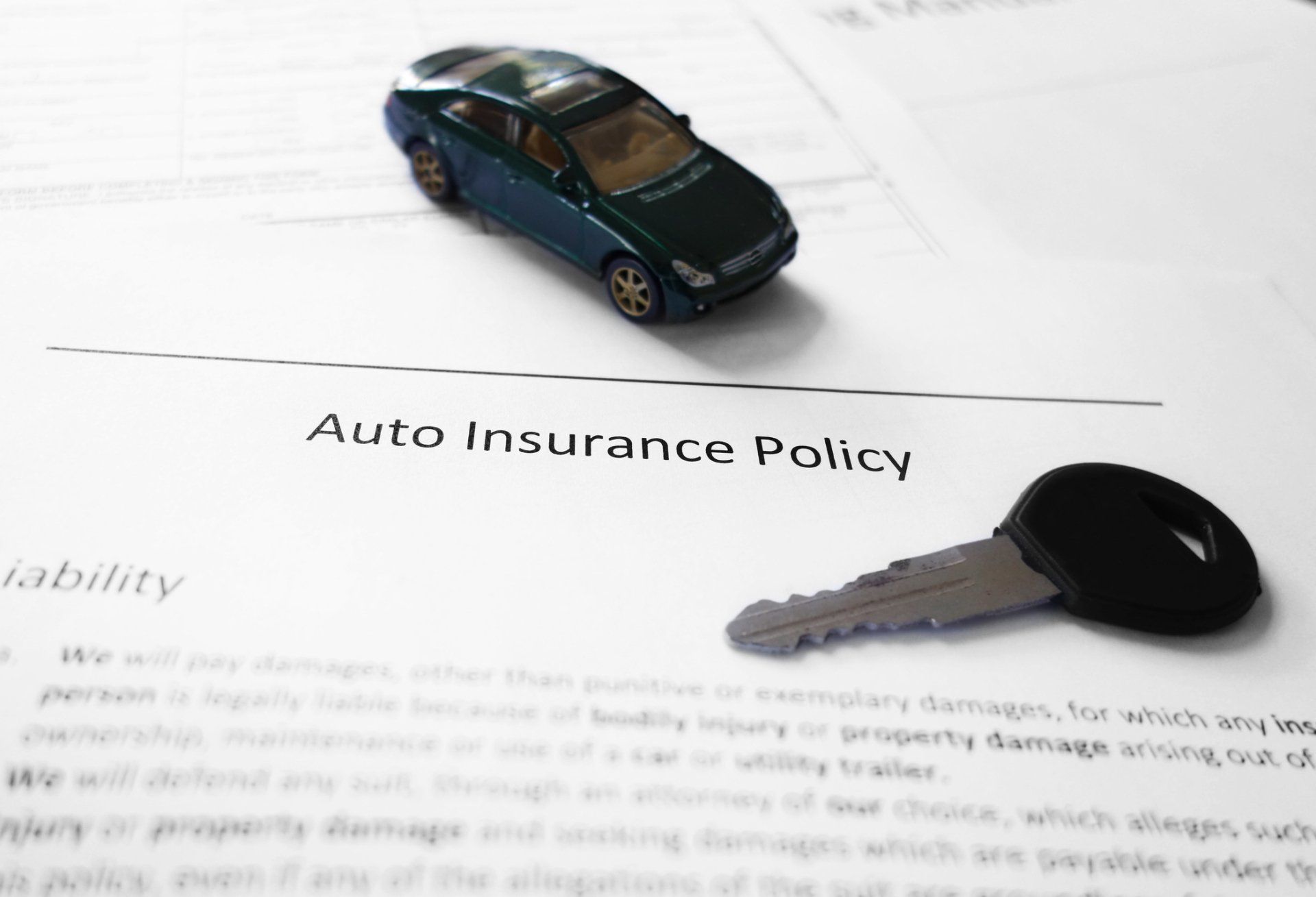 Toy car, key, and auto insurance policy on a white surface.