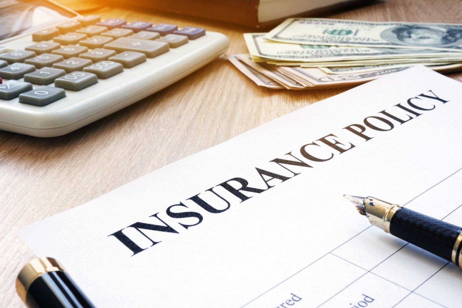 Insurance policy document with calculator, money, and pen on a desk.
