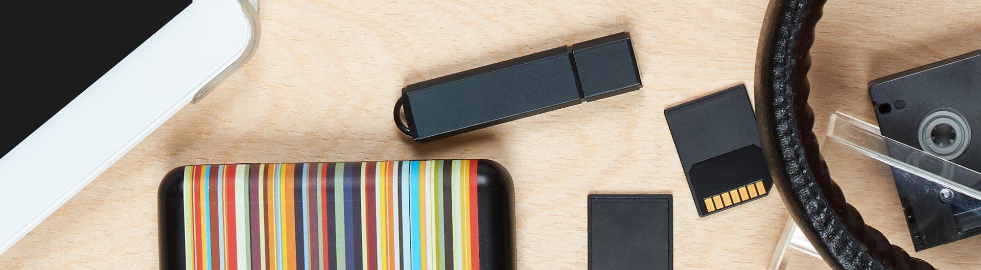Dispositivi elettronici su un tavolo di legno, tra cui una chiavetta USB, una scheda di memoria e degli smartphone.