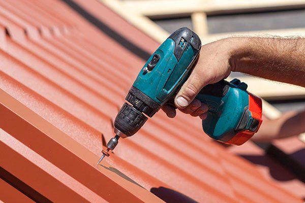 Worker on roof with electric drill installing red metal tile - Roofing & Construction in Swansboro, North Carolina Worker on roof with electric drill installing red metal tile - Roofing & Construction in Swansboro, North Carolina