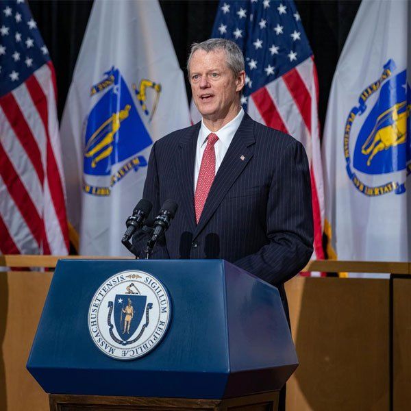 A man in a suit and tie stands at a podium in front of american flags