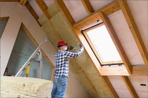 Man installing insulation in an attic, near a skylight.