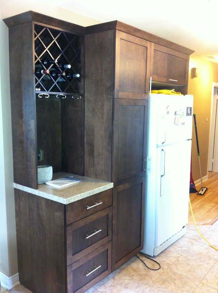 Dark wood cabinetry features a built-in wine rack, drawers, and a countertop beside a white refrigerator.