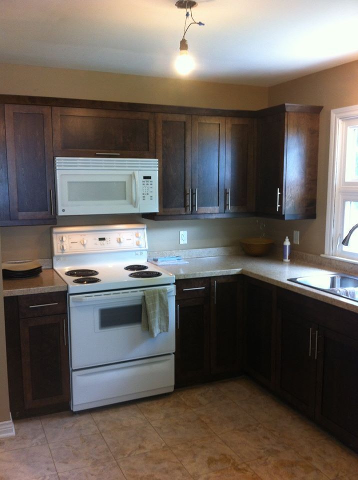 A kitchen with dark wood cabinets, a white stove and microwave, and light-colored countertops under a single pendant lamp.