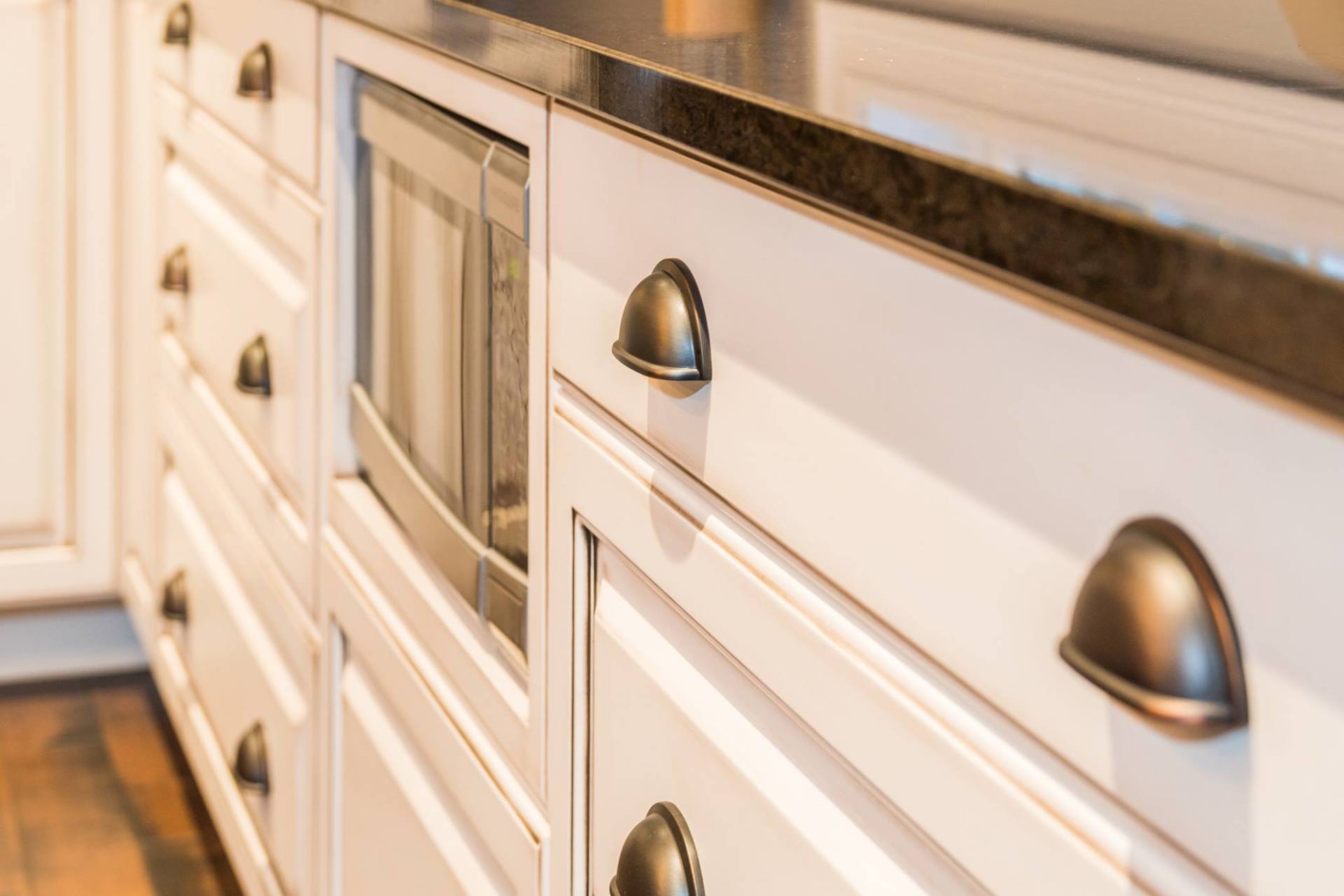 White kitchen cabinetry with dark cup-style hardware and a built-in microwave, set under a dark countertop.