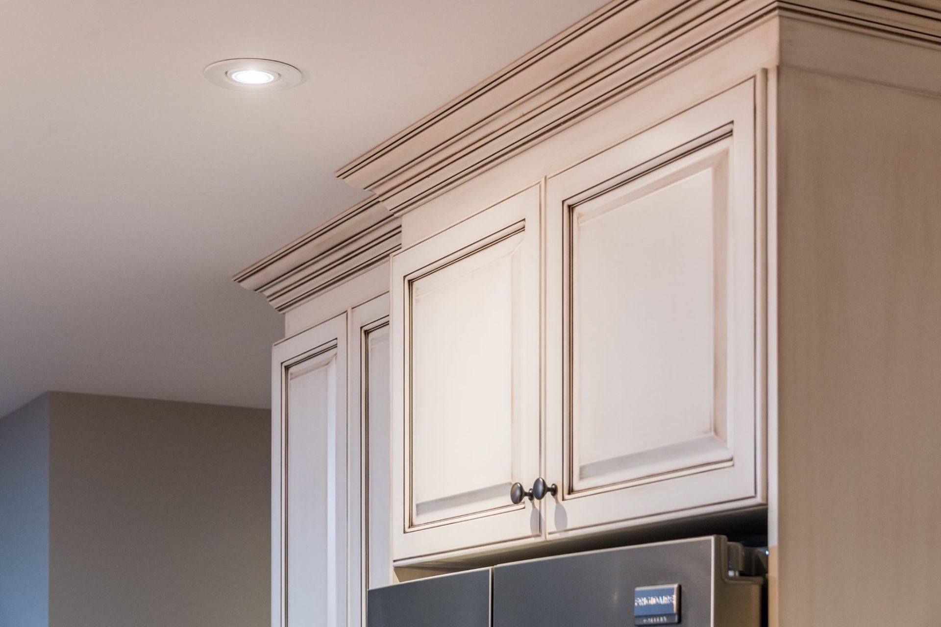 Cream-colored kitchen cabinets with crown molding installed above a stainless steel refrigerator.