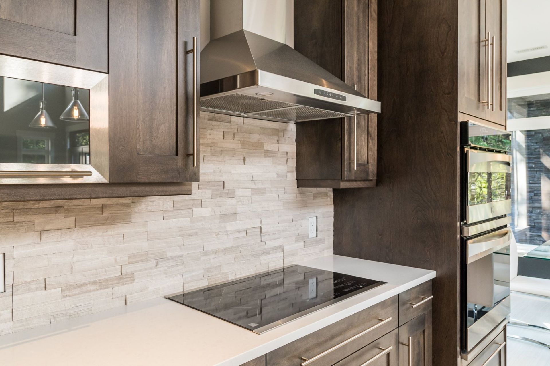 Modern kitchen with dark wood cabinets, white stone tile backsplash, stainless steel range hood, and induction cooktop.