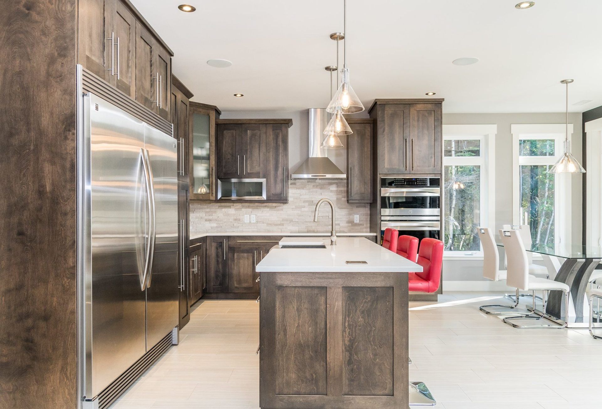 A modern kitchen featuring dark wood cabinets, a stainless steel refrigerator, a white island, and red stools.