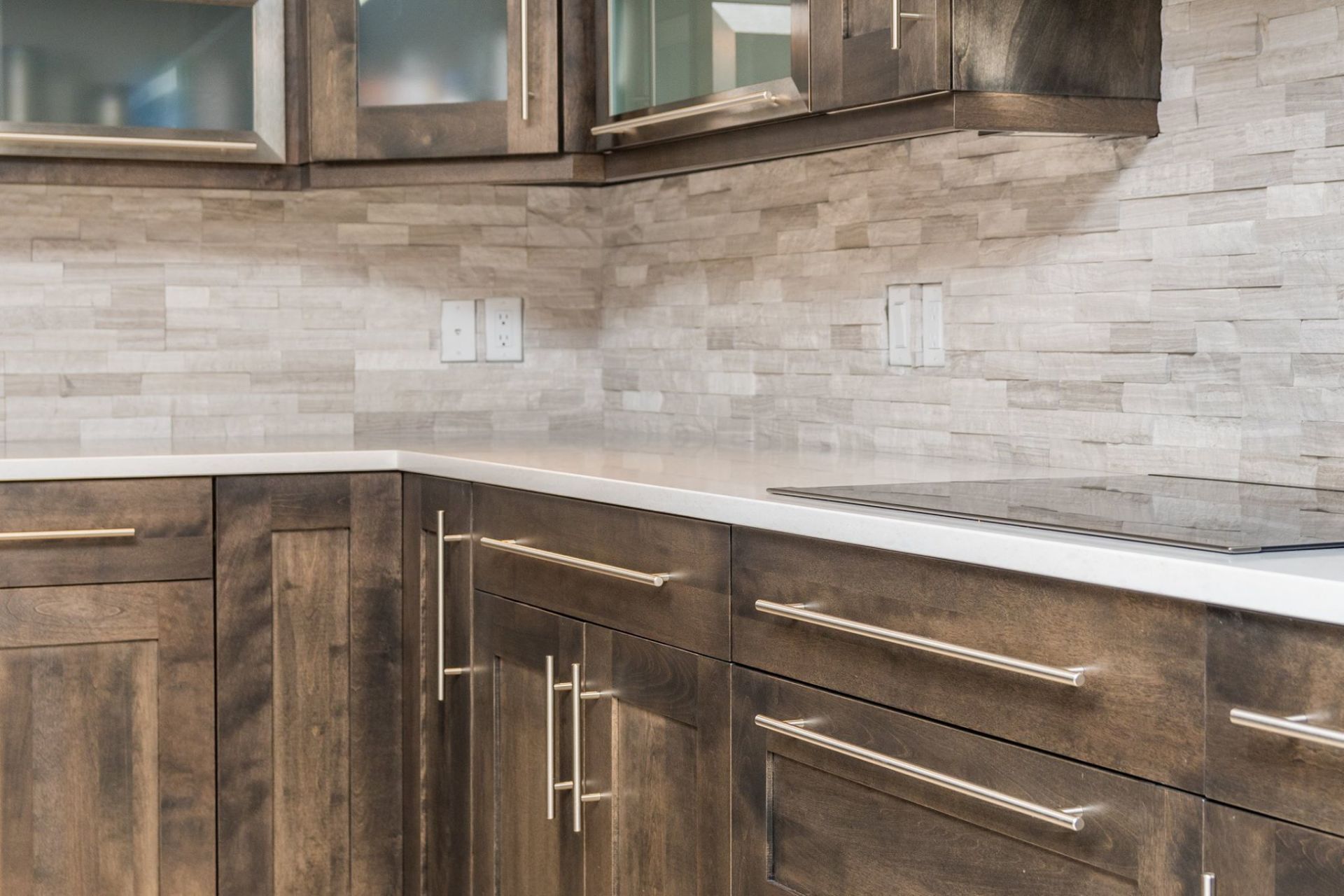 A kitchen corner with rustic wood cabinets, a white countertop, and a textured, light-colored stone backsplash.