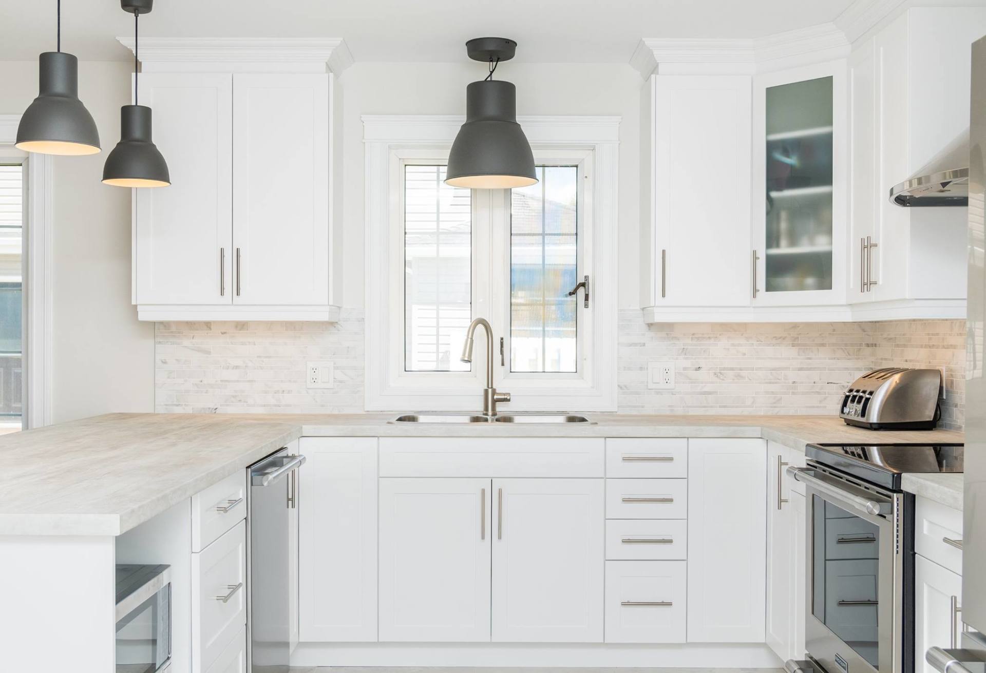 A bright kitchen featuring white cabinets, stainless steel appliances, light wood-look countertops, and hanging pendants.