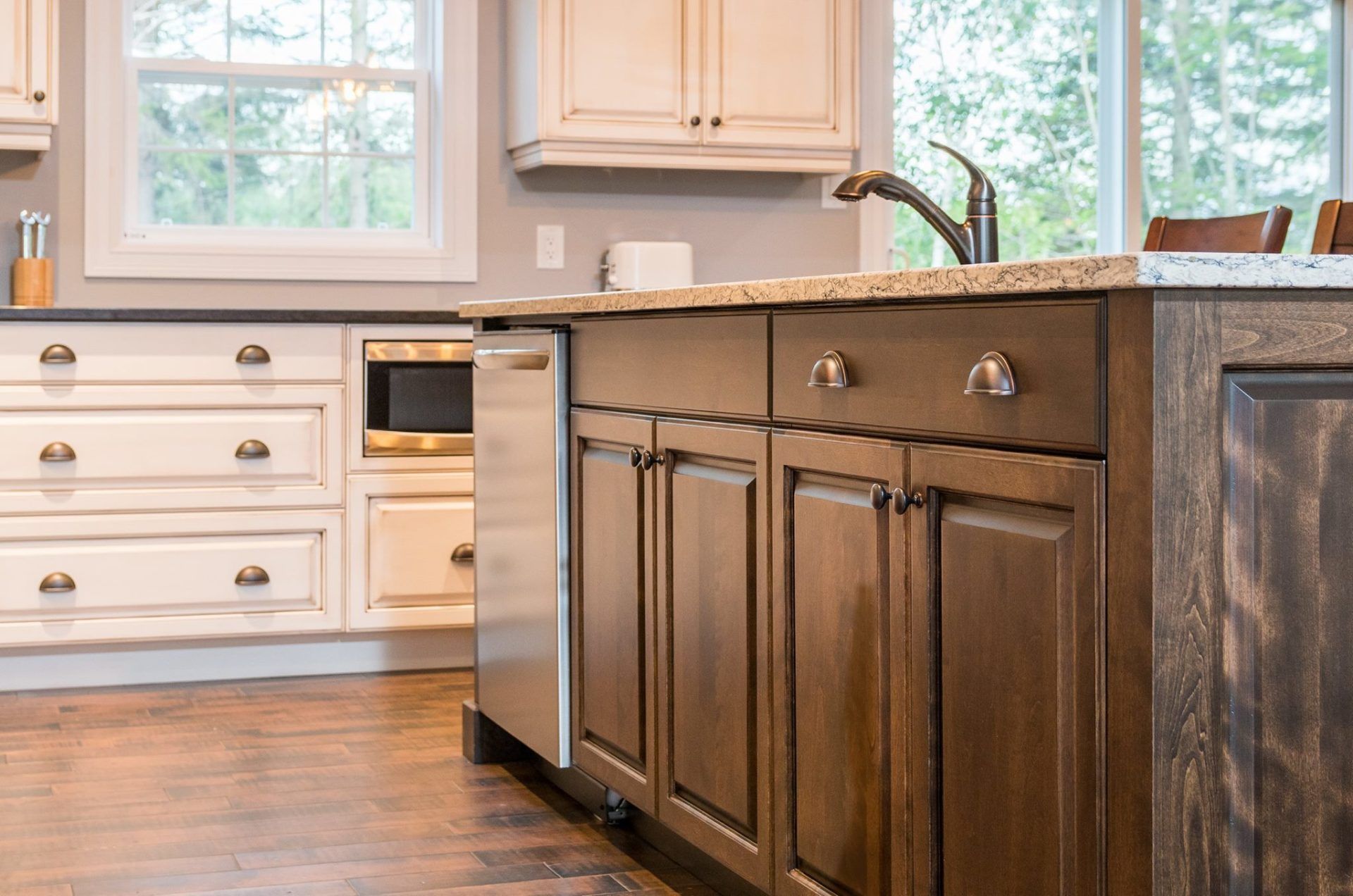 A modern kitchen featuring a dark wooden island with cabinets, a granite countertop, and white cabinetry in the background.