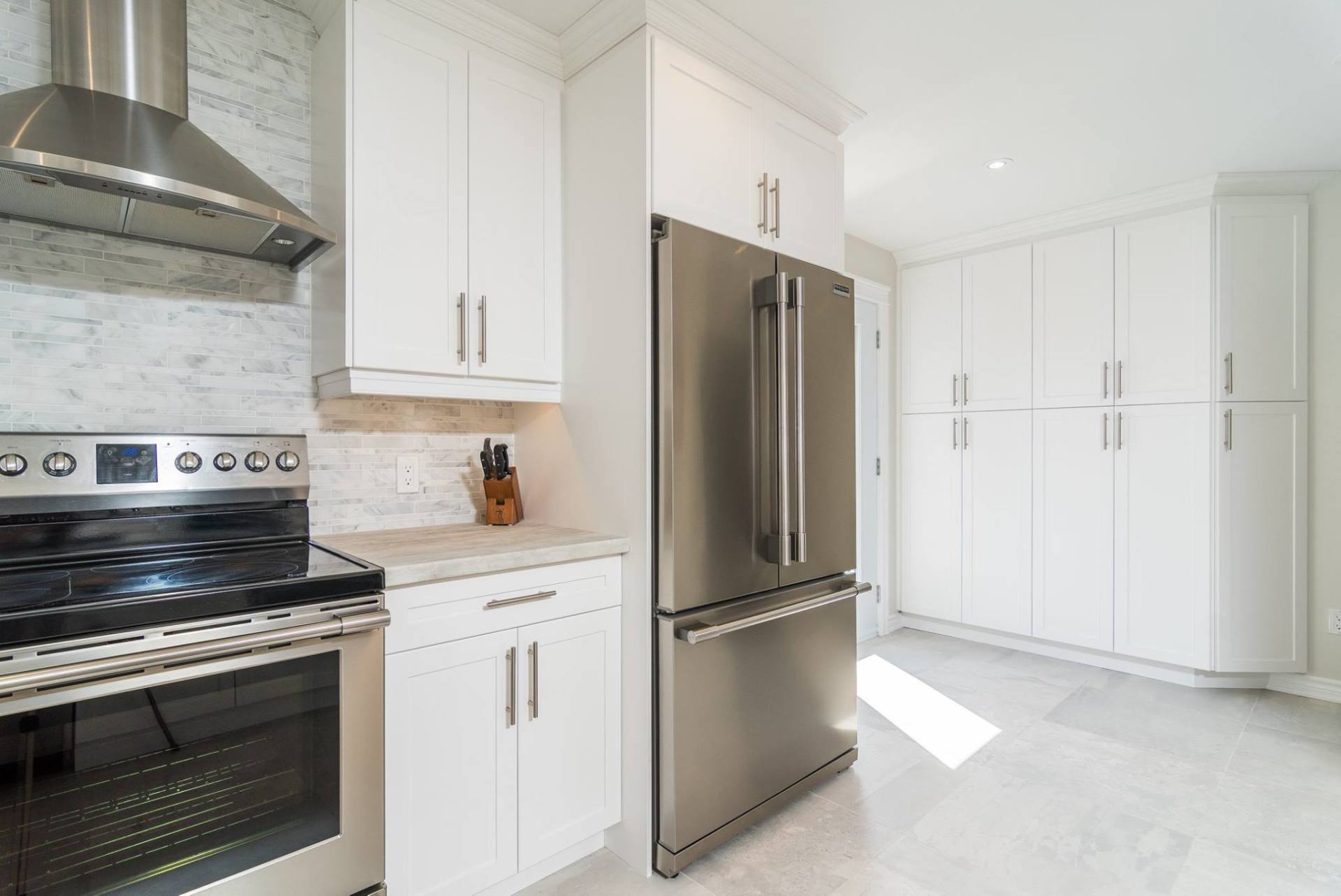 Modern kitchen with white cabinets, a stainless steel stove with a range hood, and a stainless steel refrigerator.