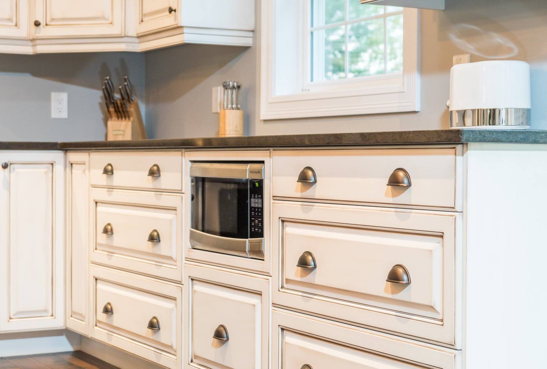 Off-white kitchen cabinets with bronze cup pulls, a built-in microwave, and dark countertops.
