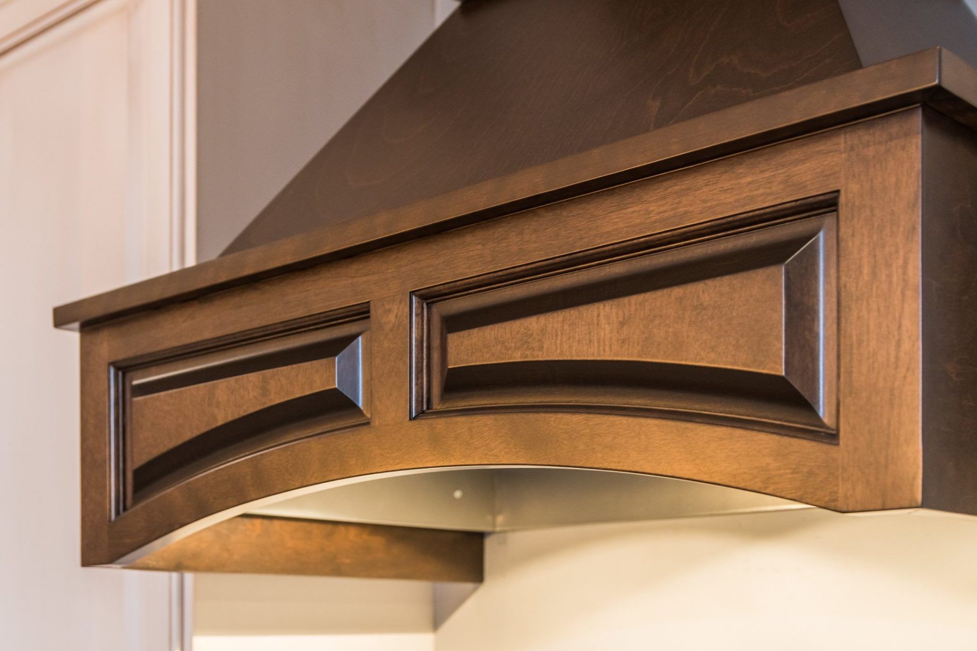 A dark wooden range hood with an arched design and recessed panels in a kitchen setting.