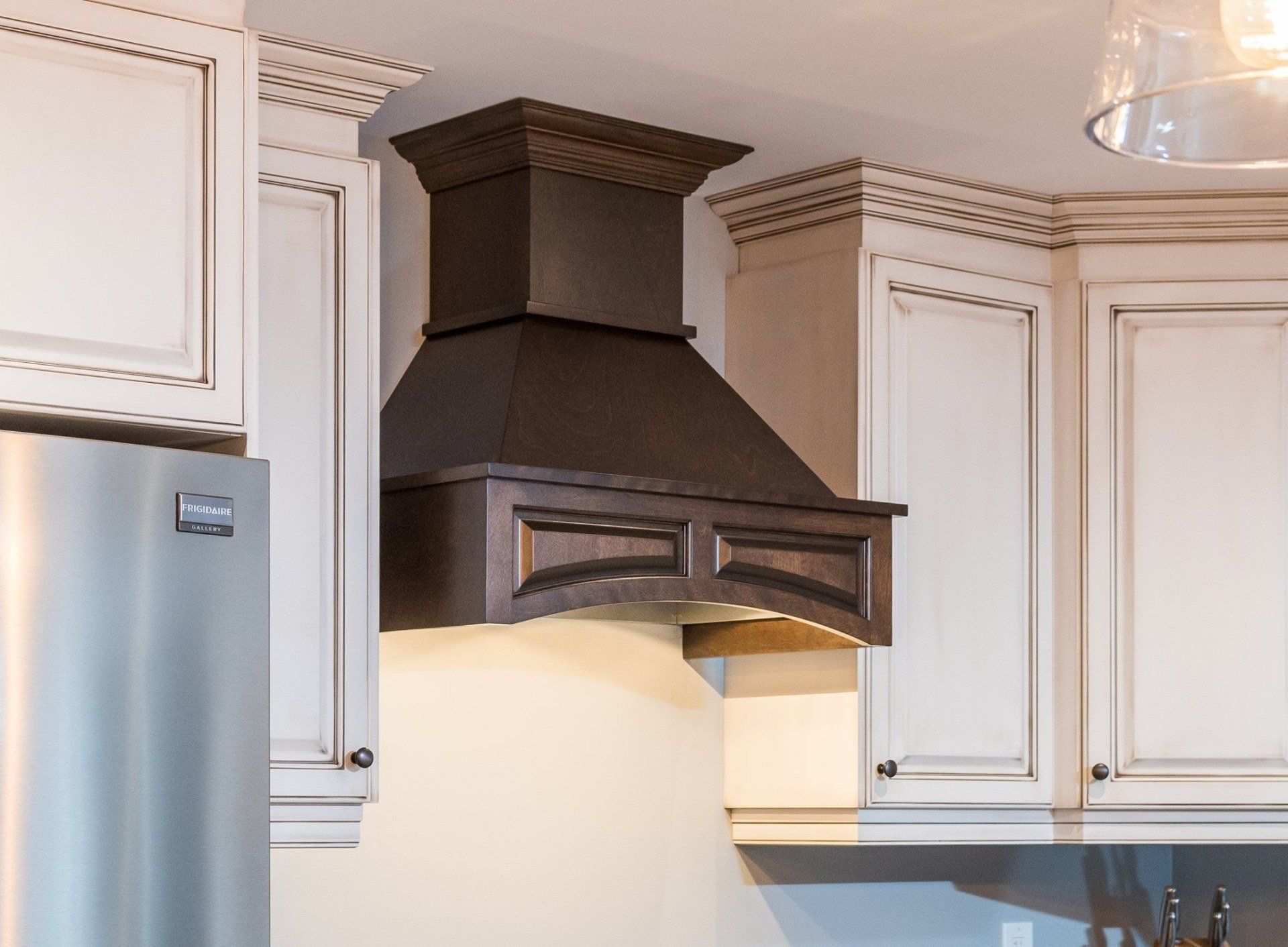 A dark brown wooden range hood is installed between white cabinets in a kitchen.