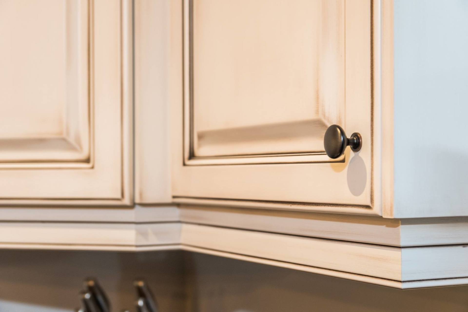 Close-up of off-white kitchen cabinets with a dark, round knob and a small, circular adhesive bumper underneath.