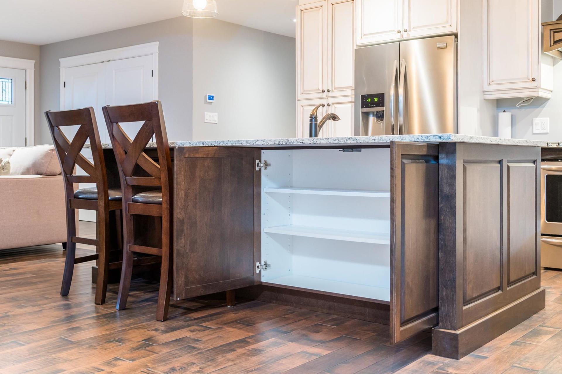 A kitchen island with two wooden chairs in front of an open cabinet showing empty white shelves.