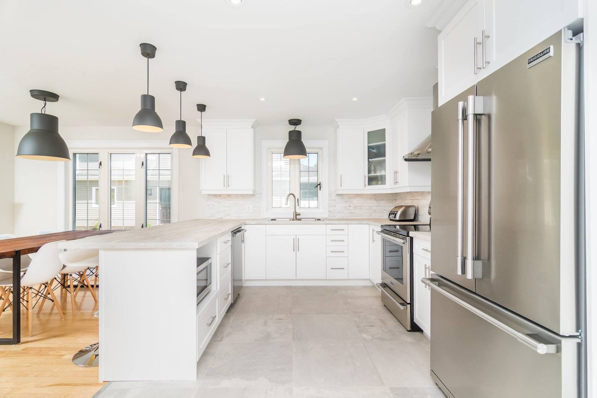 A bright, modern kitchen with white cabinets, stainless steel appliances, and large black pendant lights over an island.