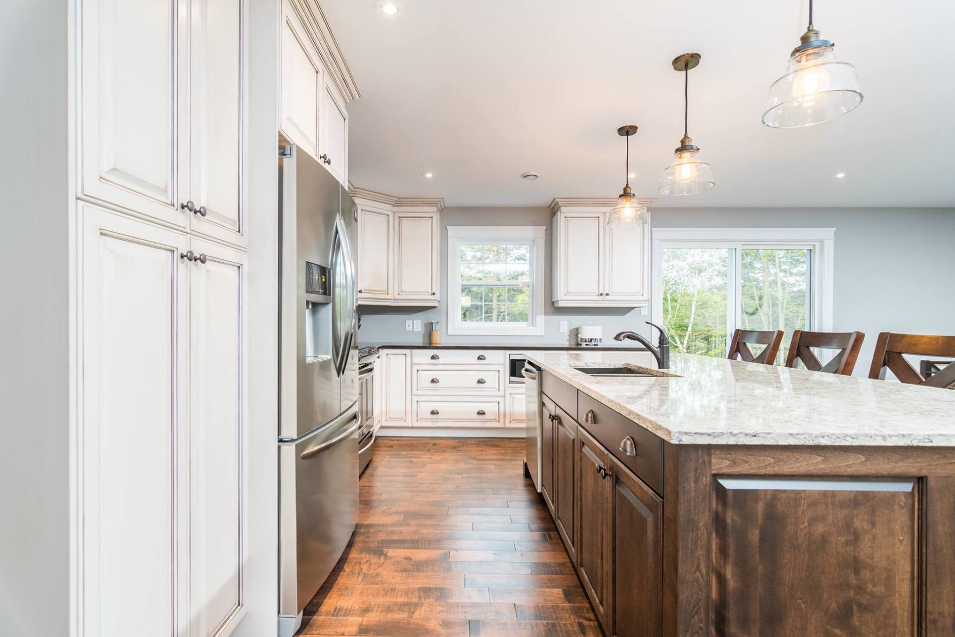 A modern kitchen featuring white cabinets, dark wood island, stainless steel refrigerator, and granite countertops.