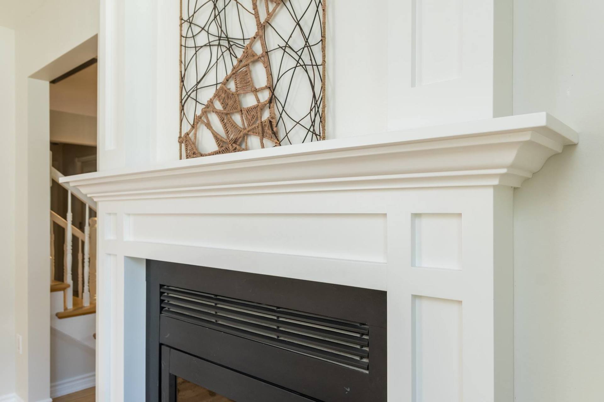 A white fireplace mantel with decorative panels and a black firebox, featuring a metal wire art piece resting on top.