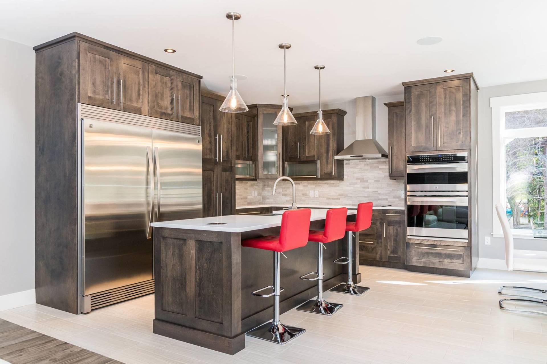 A modern kitchen features dark wood cabinets, stainless steel appliances, a center island with three red stools, and lighting.