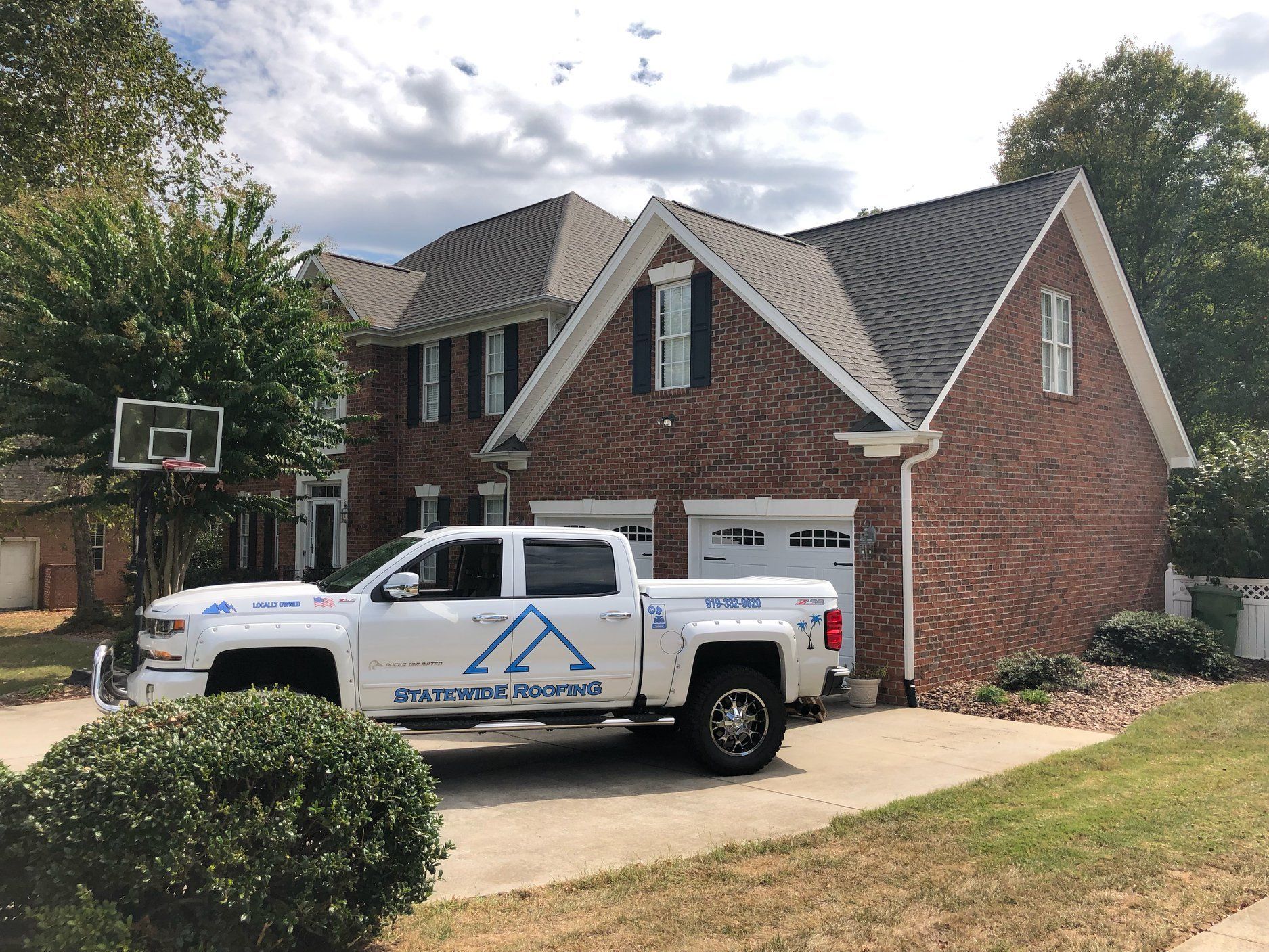 a white truck with label of Statewide Roofing parked in front of a large brick house .