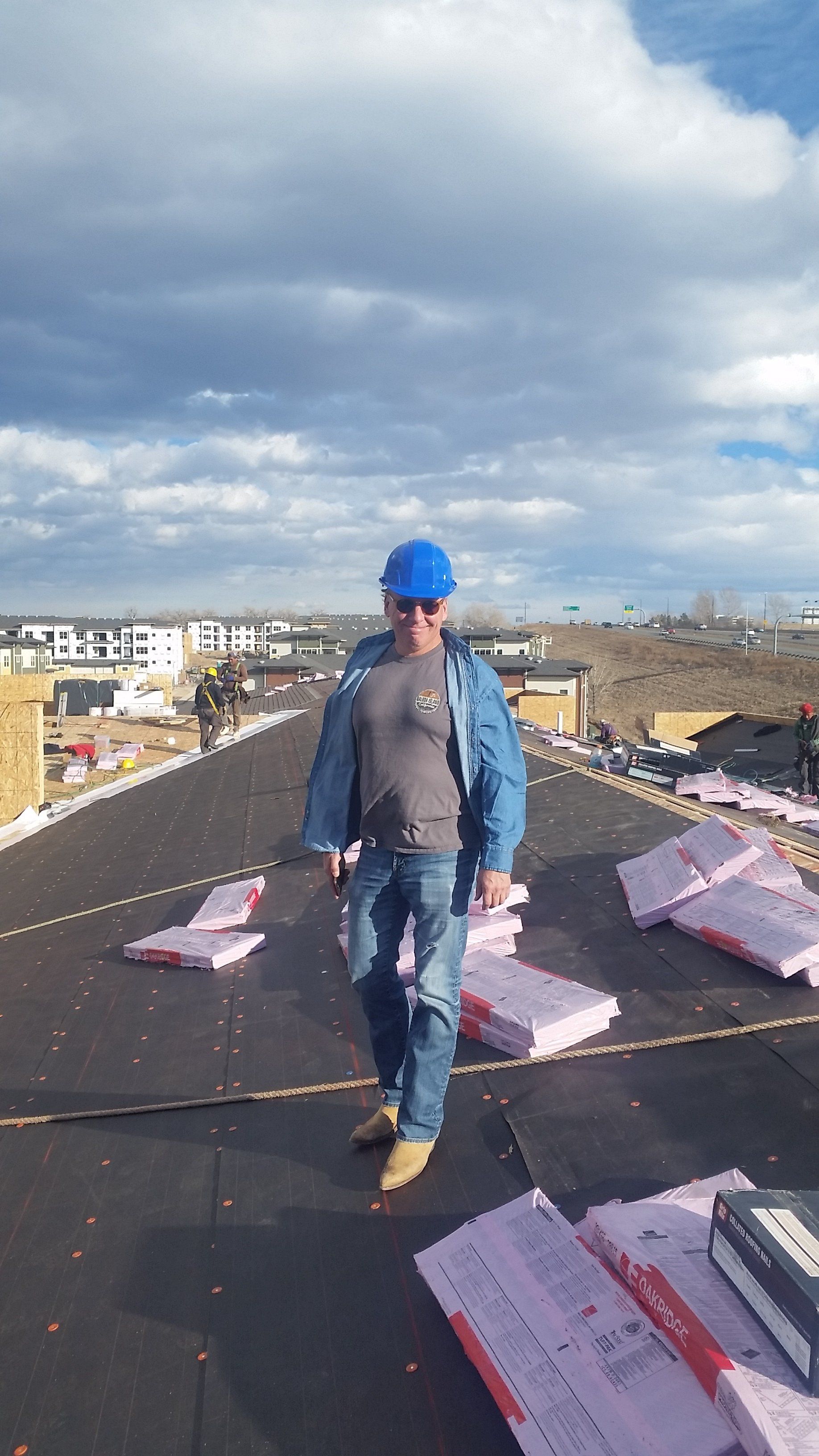 a man in a blue hard hat is standing on top of a roof .