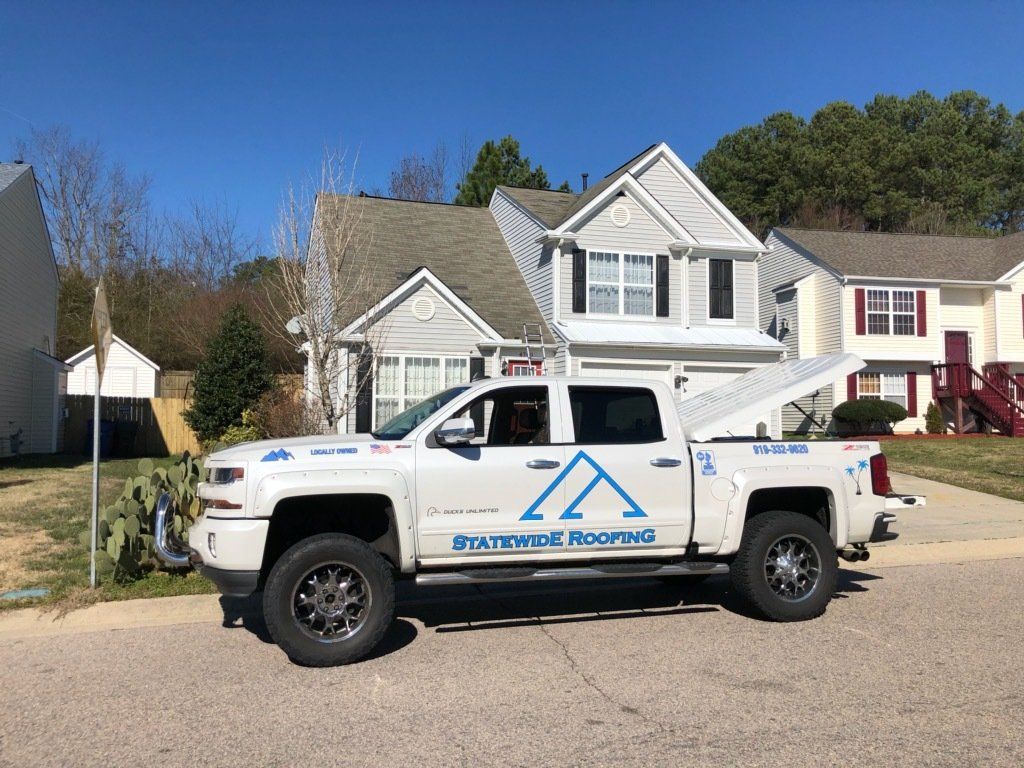 a white Statewide Roofing truck is parked in front of a house .