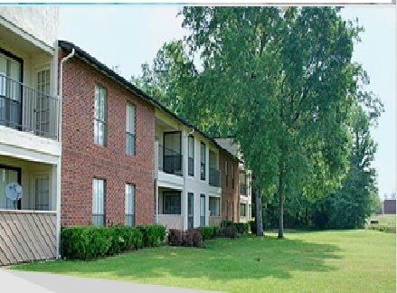 Two-story brick apartment building with green lawn and trees.
