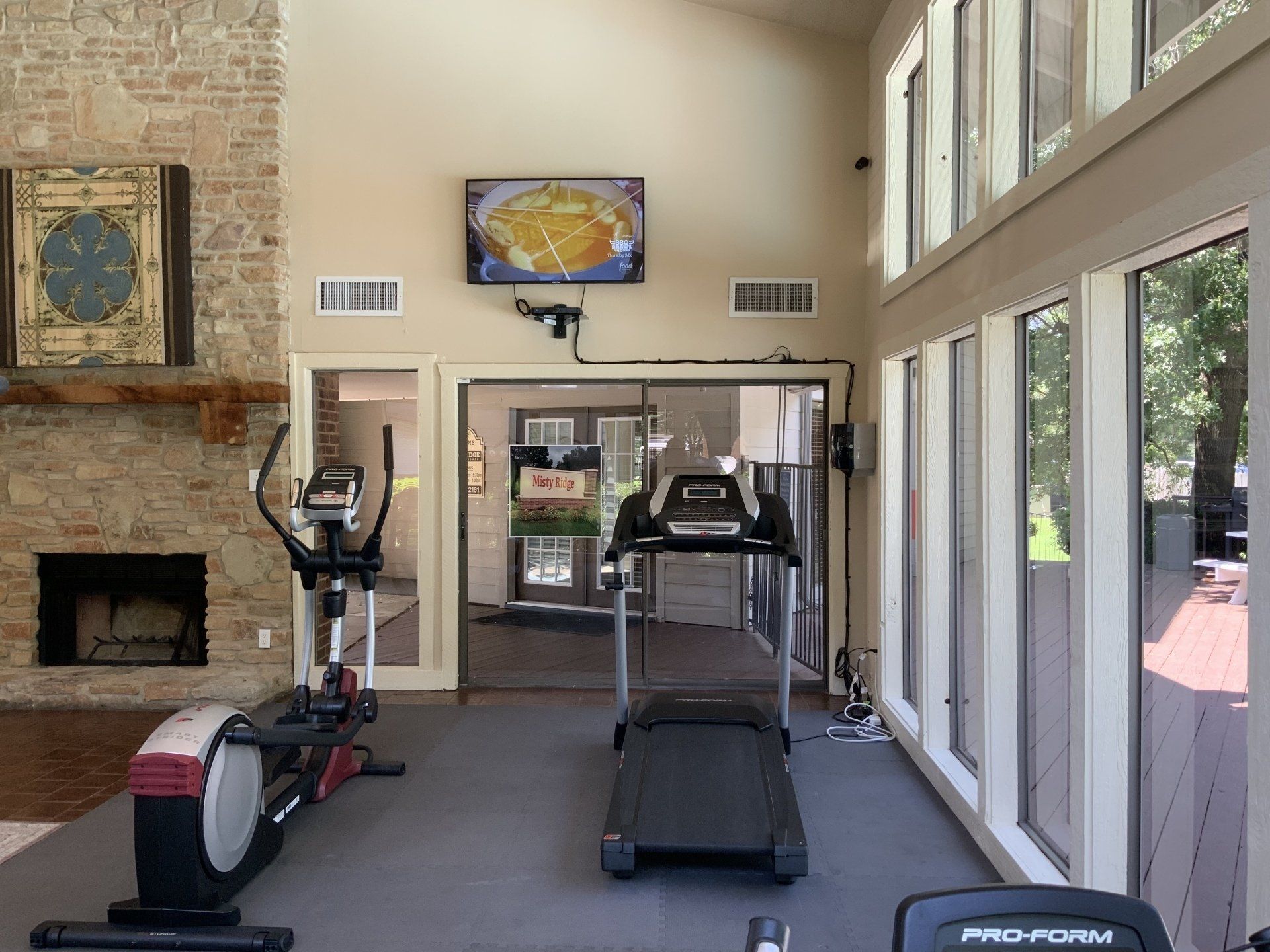 Gym with exercise equipment, TV, fireplace, and windows.