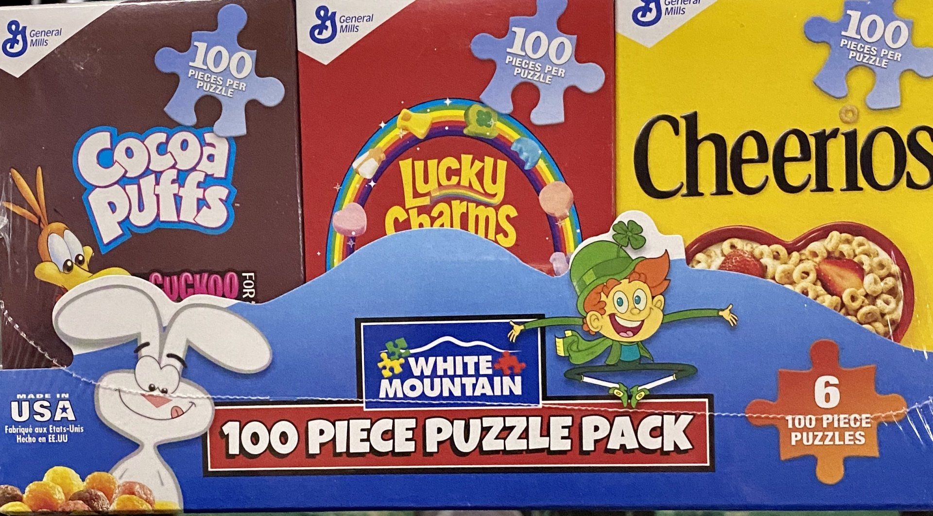White Mountain 6-pack 100-piece cereal-themed jigsaw puzzles featuring Cocoa Puffs, Lucky Charms, and Cheerios boxes.