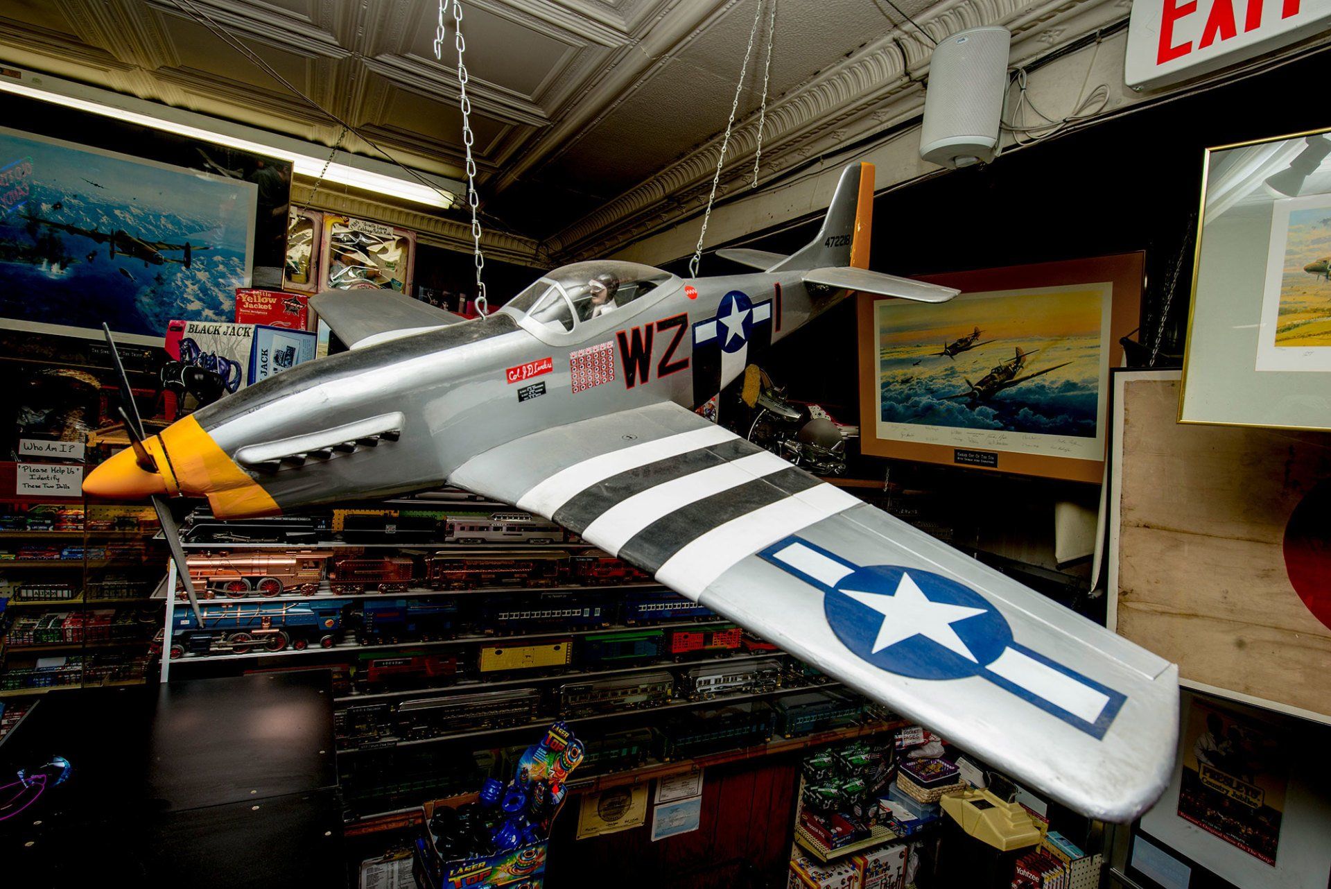 A model P-51 Mustang airplane with Invasion stripes hangs from the ceiling inside a hobby store.