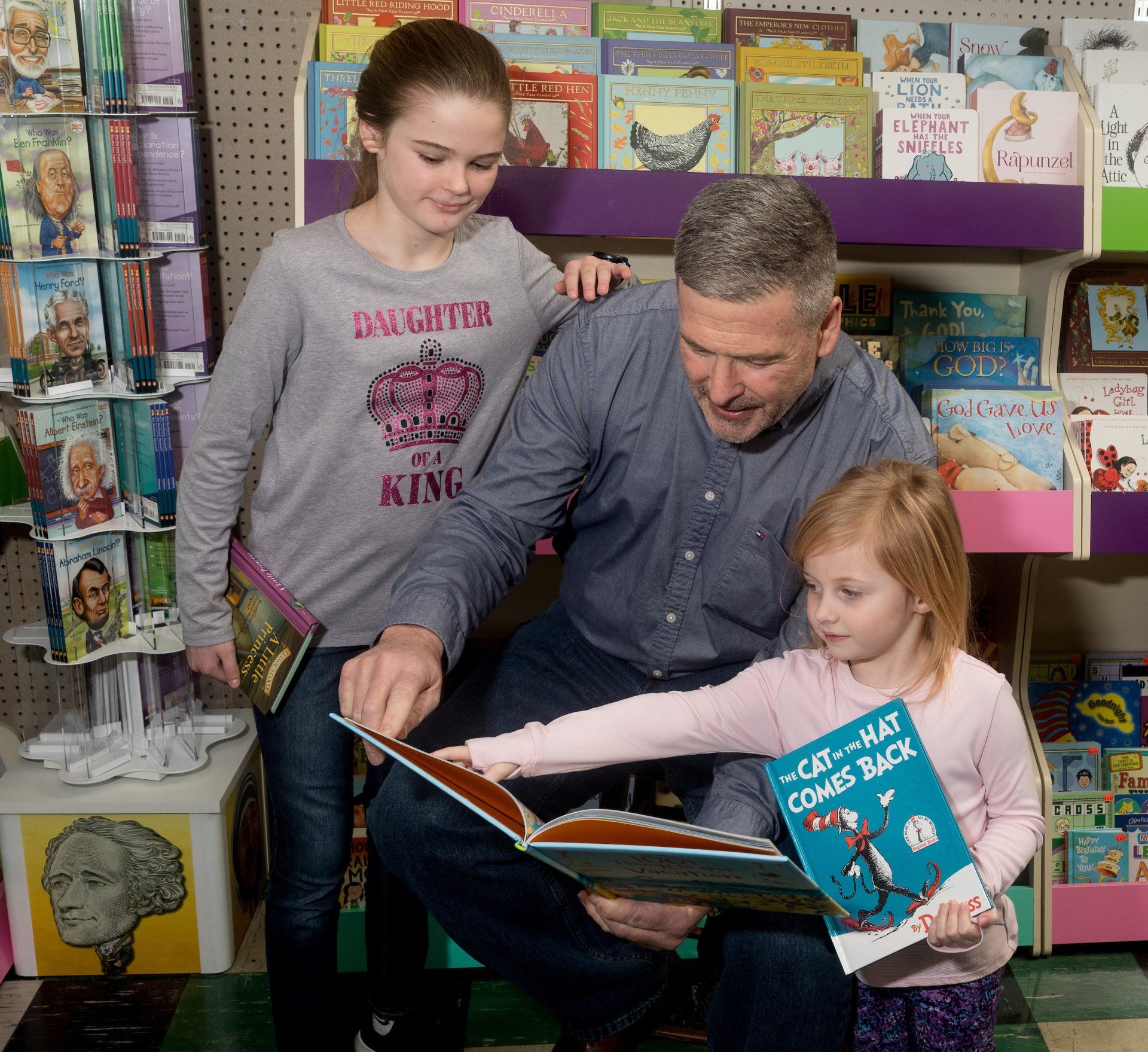 A man and two children reading a book together in a bookstore.