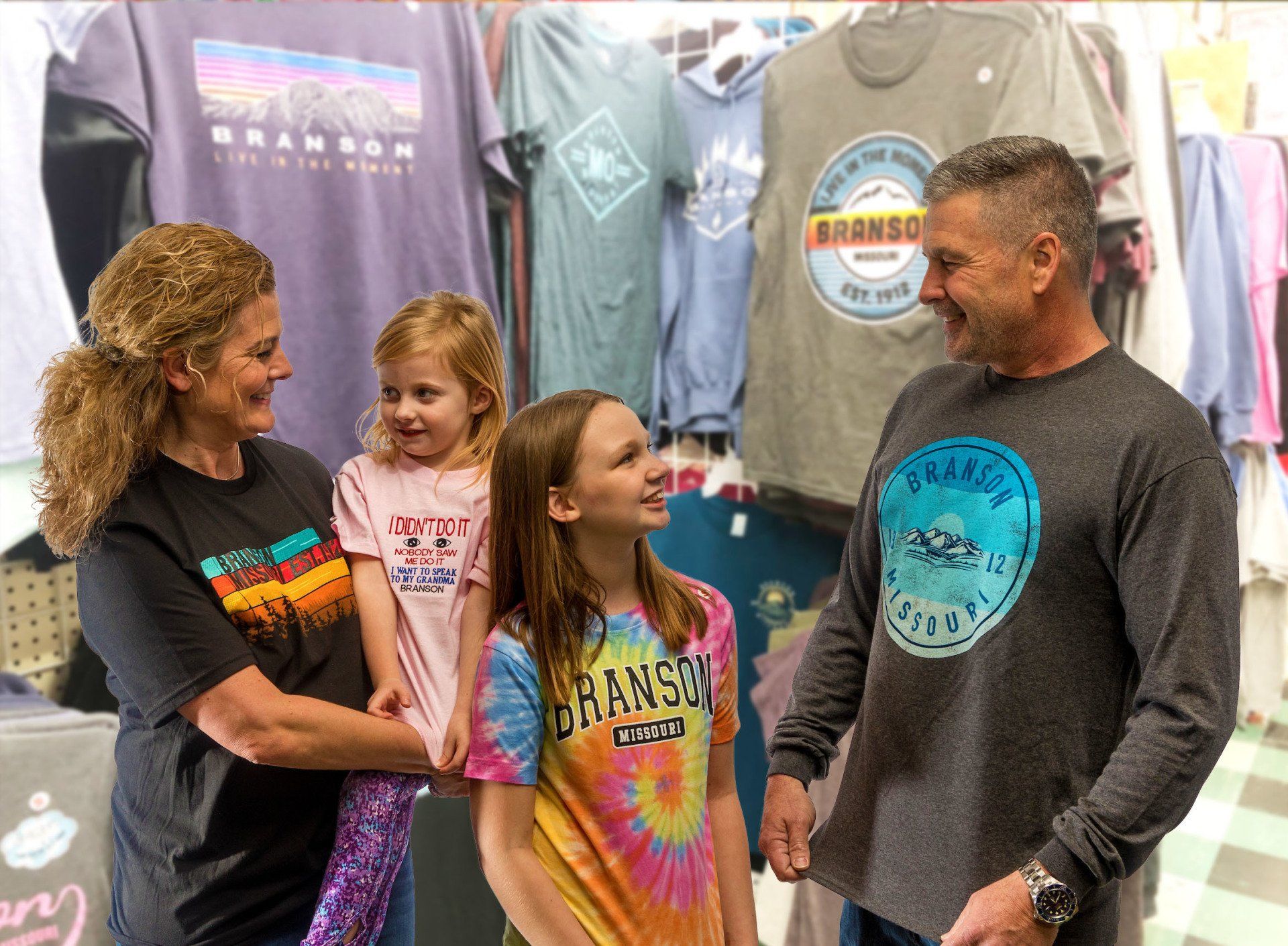 A family smiles while shopping for souvenirs in a store filled with branded clothing racks.