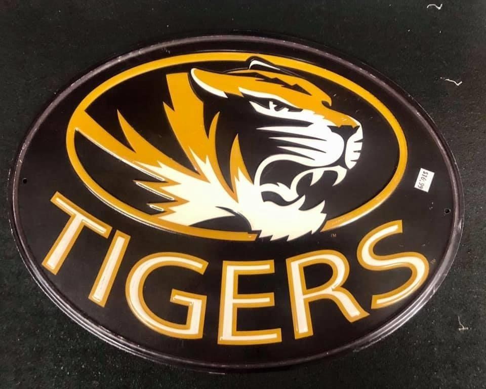 An oval sign with a black background, a stylized gold and black tiger head logo, and the word 
