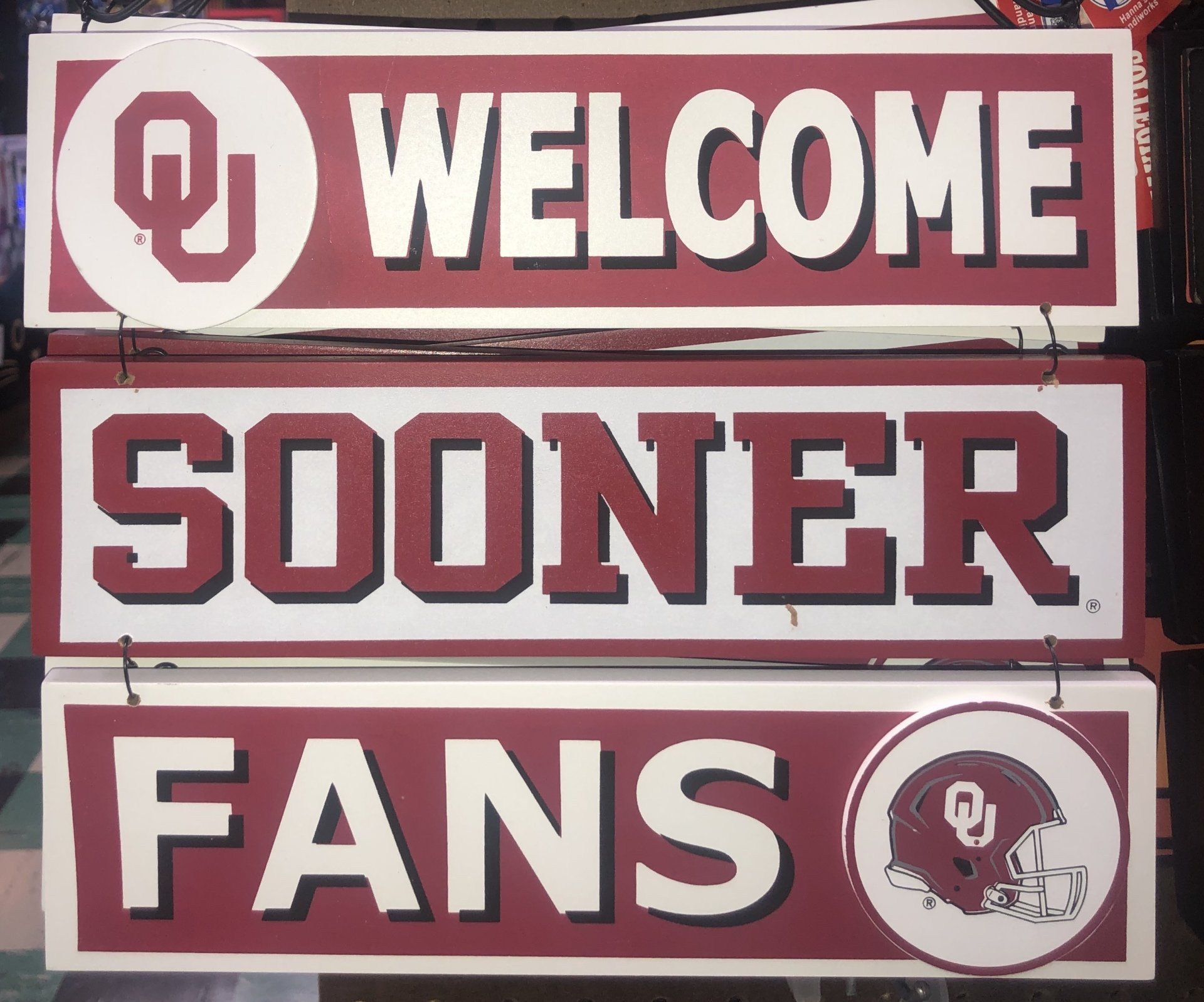 Three stacked wooden signs in crimson and white text read 