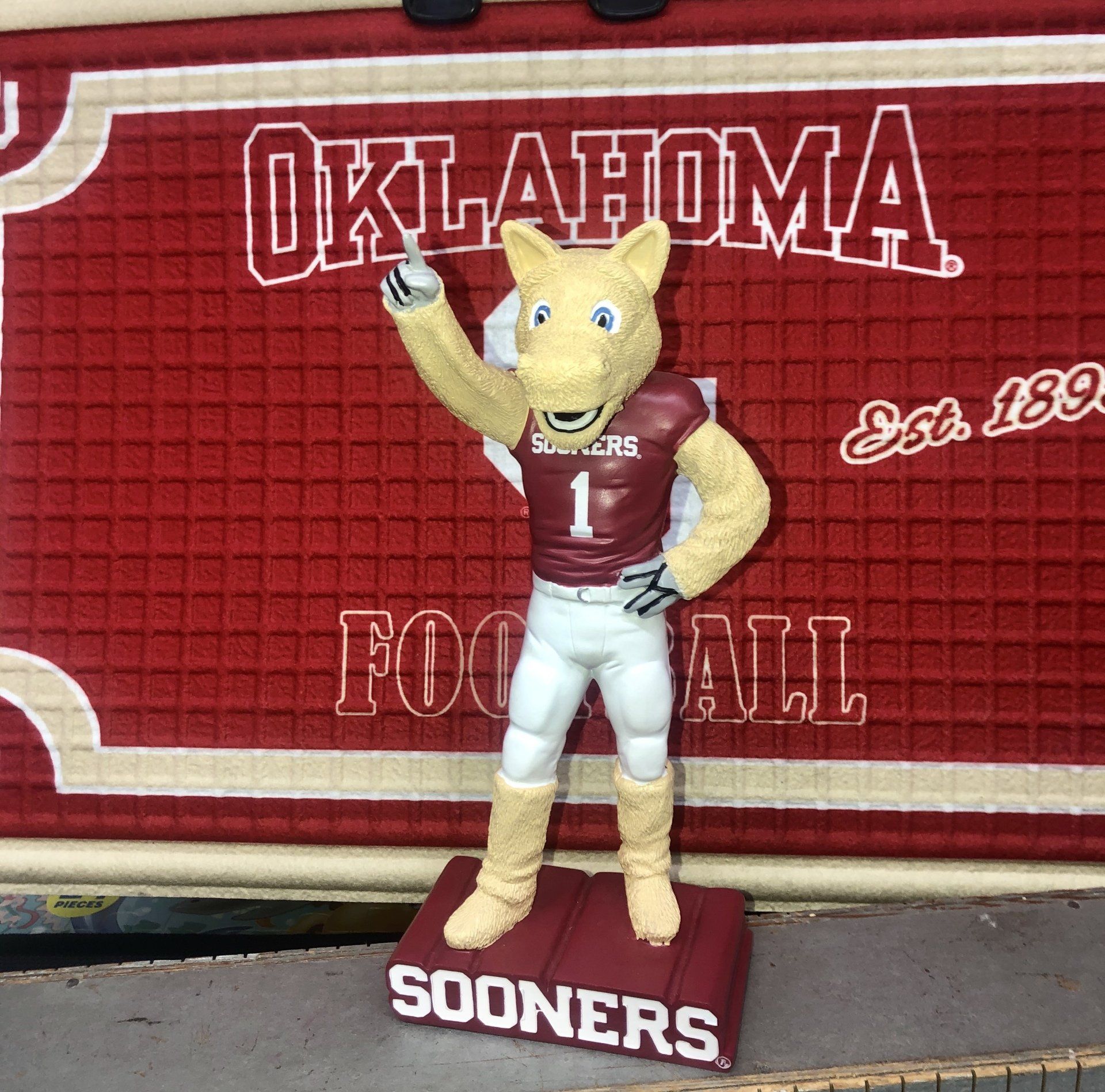 A Sooner Schooner mascot bobblehead wearing a crimson #1 jersey, standing on a 