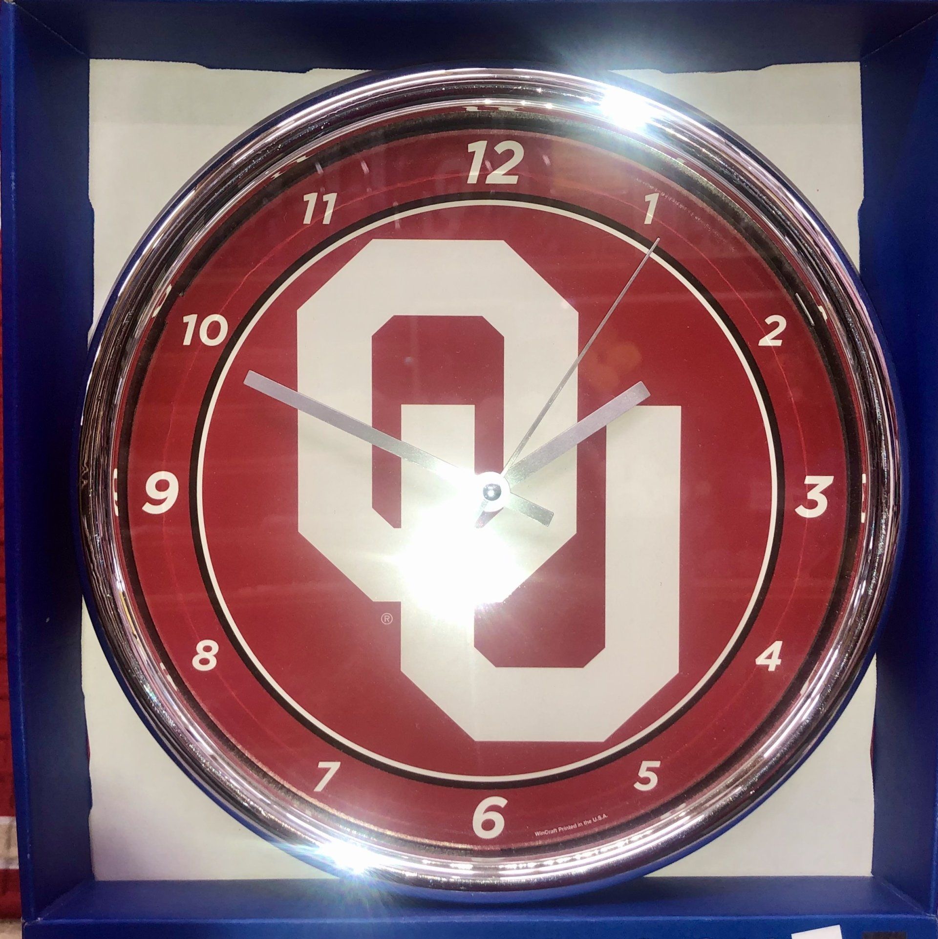 A round wall clock with a crimson background and the white University of Oklahoma 