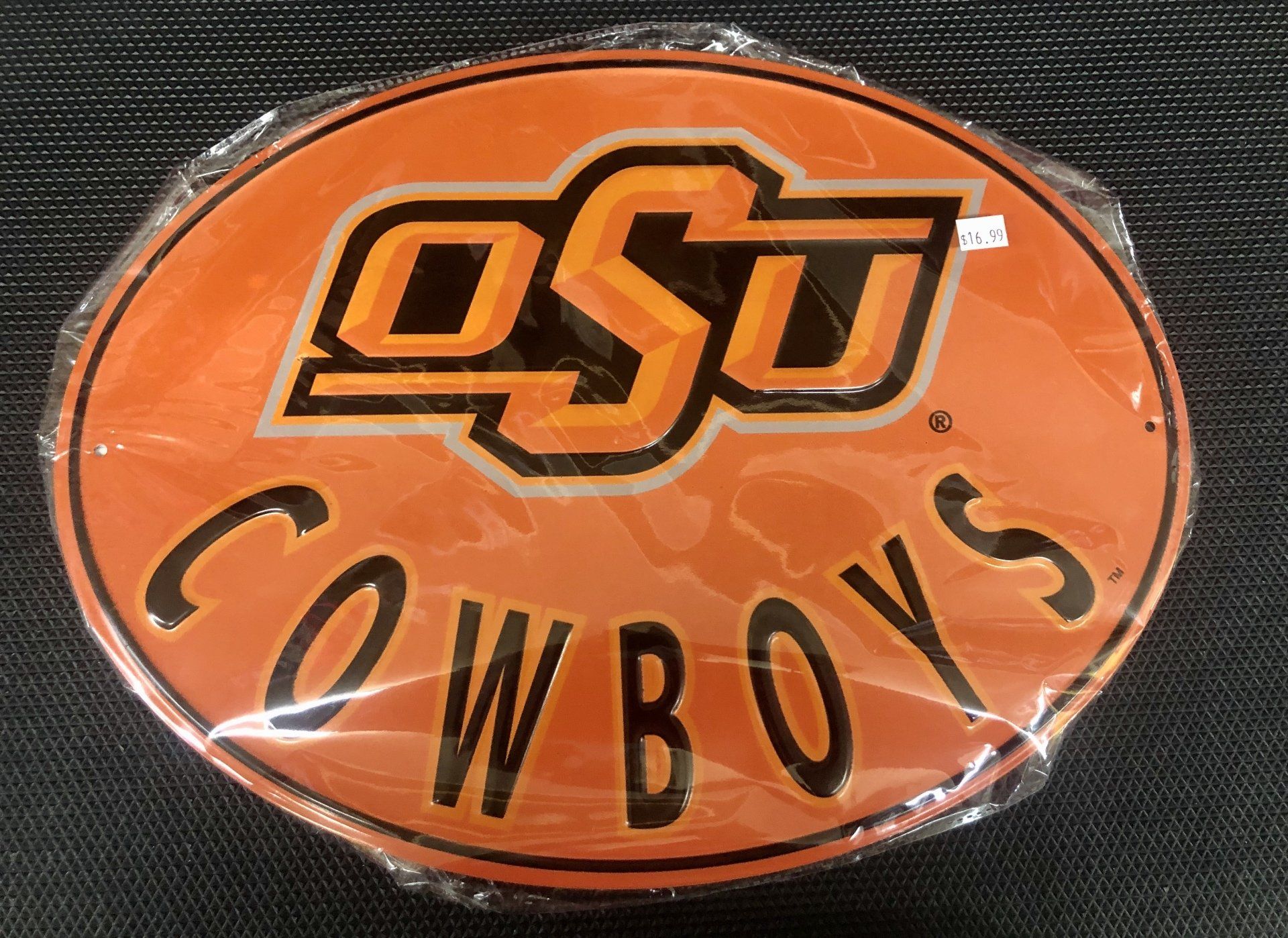 An oval-shaped Oklahoma State University sticker in orange and black, still inside its clear plastic packaging.