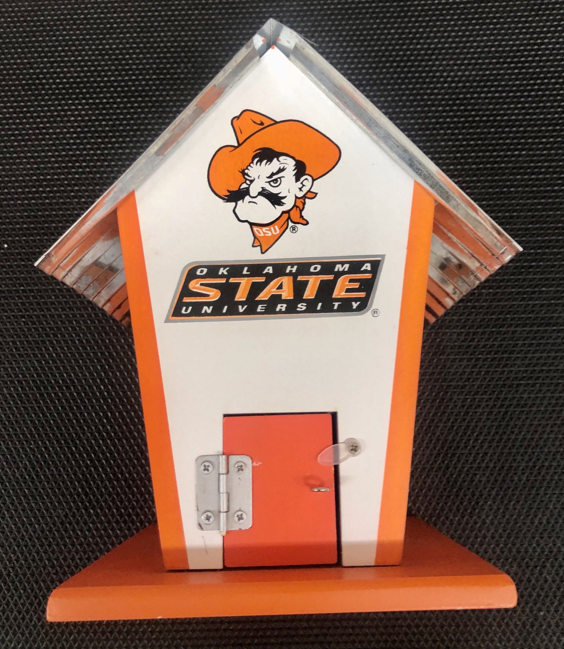 An Oklahoma State University branded wooden birdhouse with orange and white paint, featuring the mascot on the front.